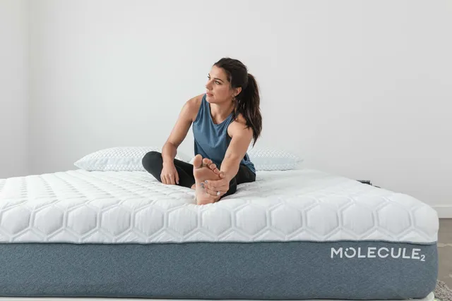 Alex Morgan stretching barefoot while seated on a mattress.