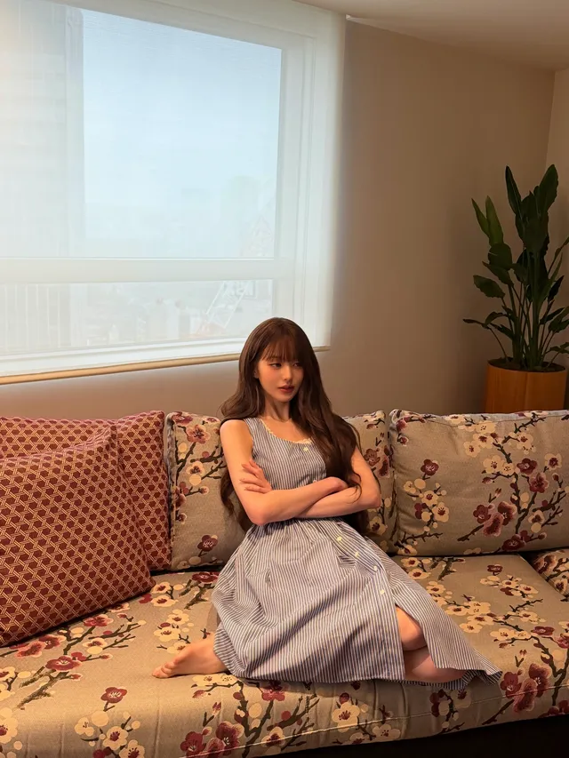 Jang Wonyoung sitting on a patterned sofa in a grey dress.
