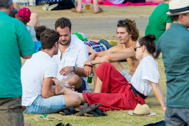 Daisy Ridley sitting with guests on grass in a red dress.