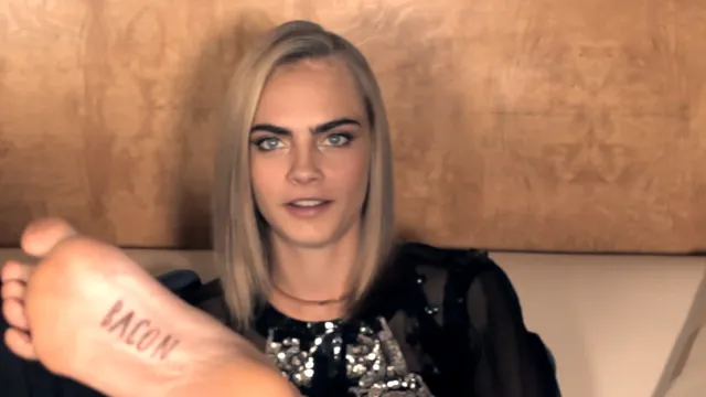 Cara Delevingne showing a foot tattoo while seated.
