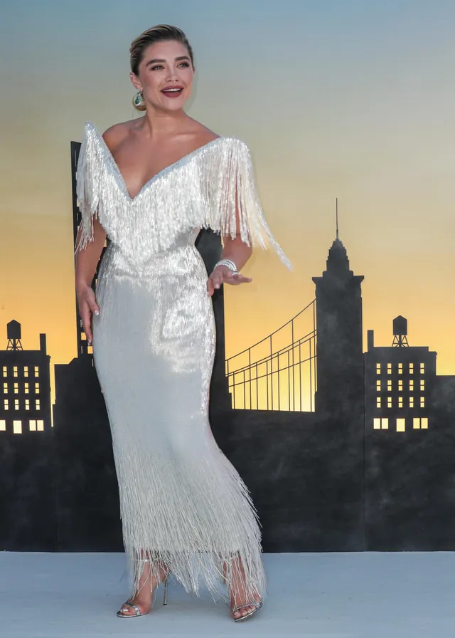 Florence Pugh posing in a silver gown and heels against a city backdrop.