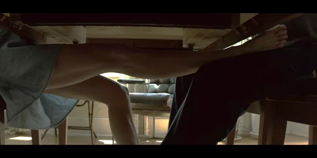 Sienna Miller sitting beside another character at a table in a scene.