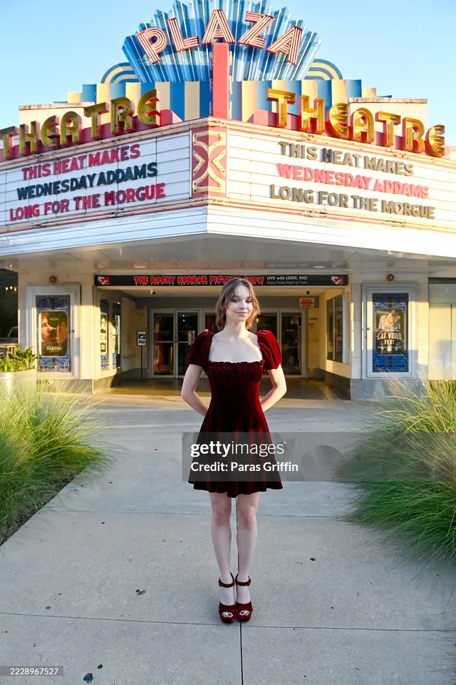 Emma Myers standing outside a theatre wearing a black dress and red heels.