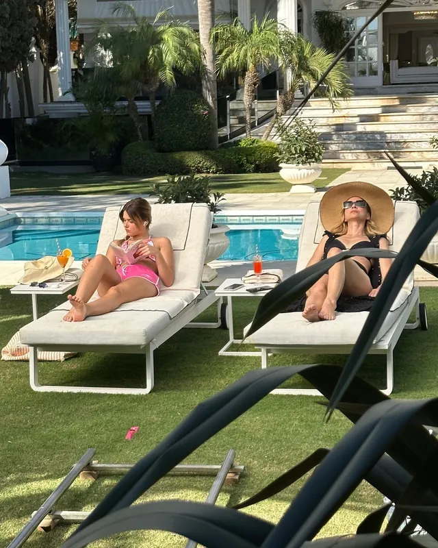 Nicole Wallace reclining barefoot in a pink swimsuit beside a pool in a scene.