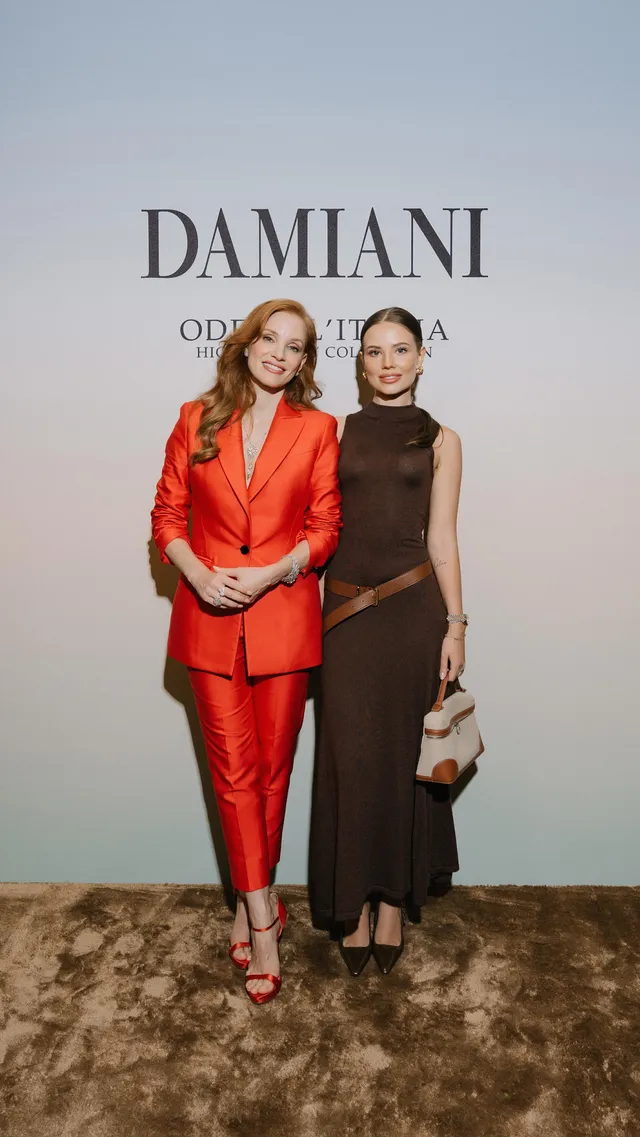 Jessica Chastain posing with a guest in a red trouser suit.