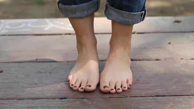 Kristen Bell with bare feet standing on a wooden deck below rolled jeans.