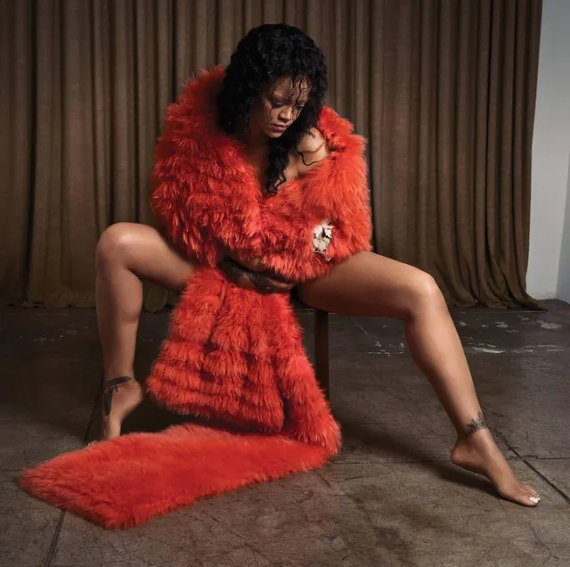 Rihanna sitting barefoot in a red robe on a wooden floor.
