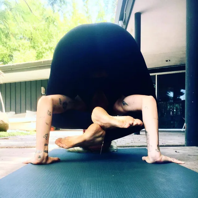Miley Cyrus holding a barefoot yoga balance on a mat.