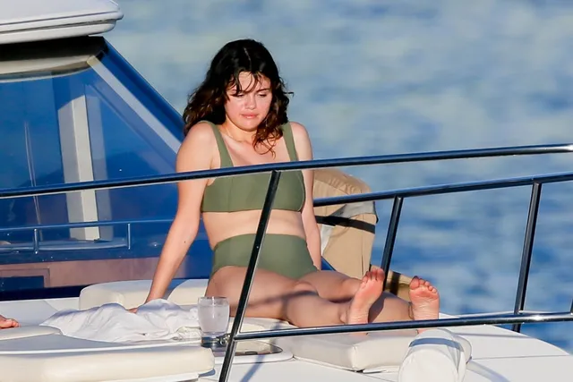 Selena Gomez sitting on a boat in a green swimsuit.