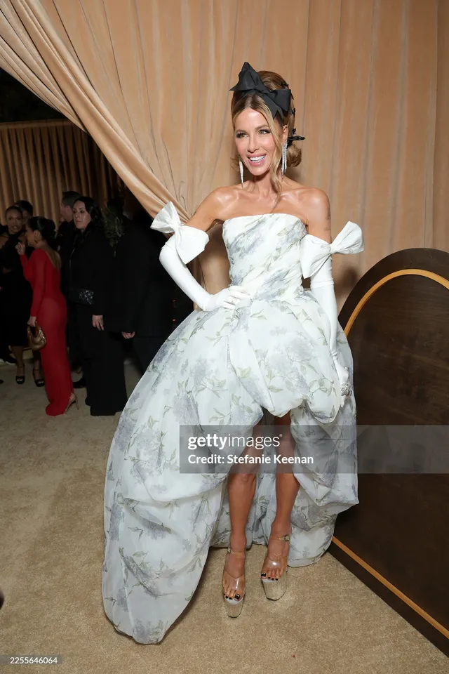 Kate Beckinsale standing in a floral dress and heels at an event.