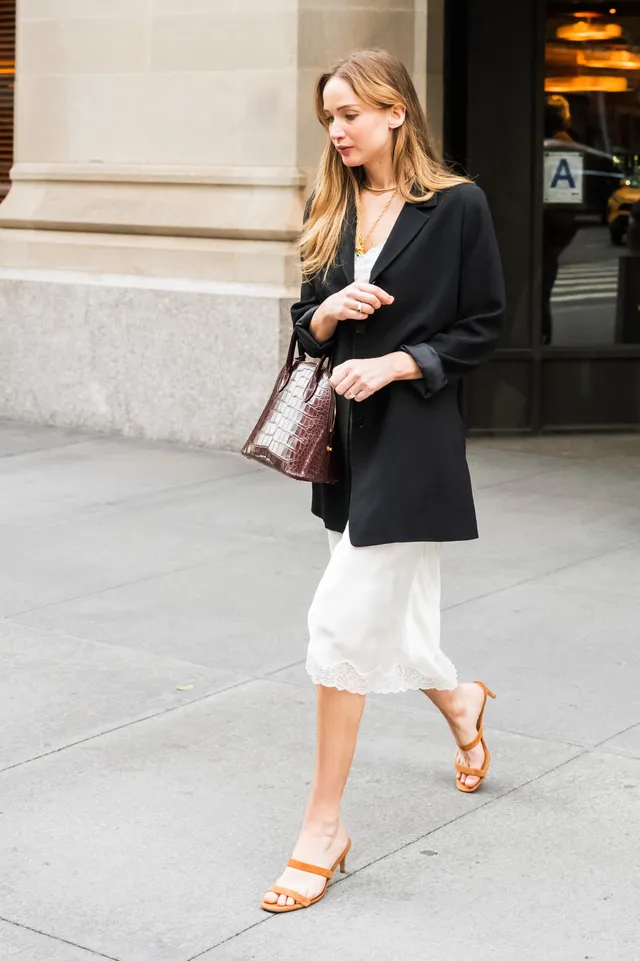 Jennifer Lawrence walking outside in a white skirt and flat sandals.