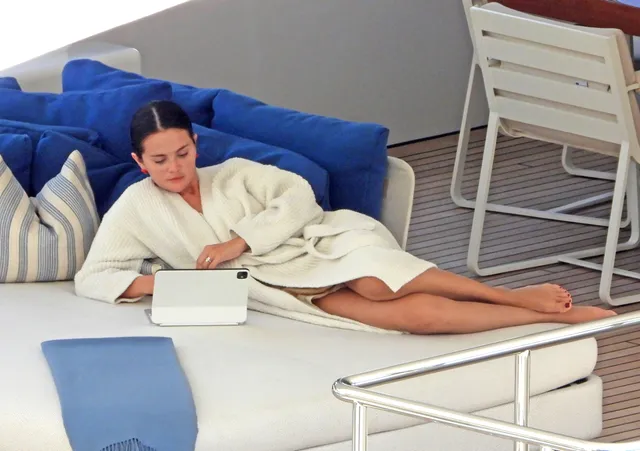 Selena Gomez reclining on a boat in a white robe.