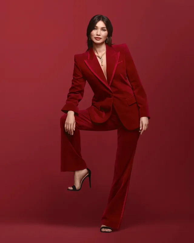 Gemma Chan posing in a red suit against a red backdrop.