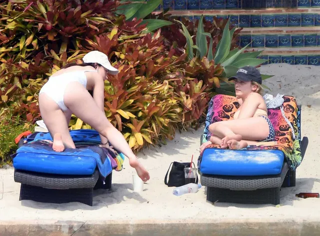 Dakota Johnson kneeling barefoot on a blue lounger beside the pool.