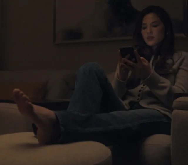 Olivia Munn sitting on a sofa with bare feet visible in a film scene.