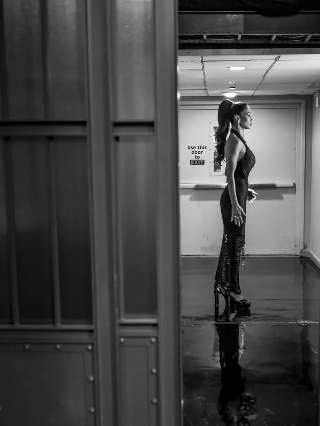 Nicole Scherzinger posing in a black gown and platform heels in a monochrome photograph.