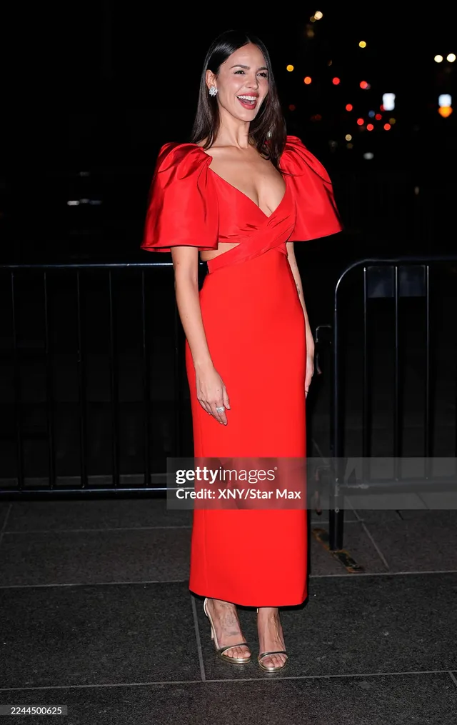 Eiza González standing outdoors in a red dress and heeled sandals.