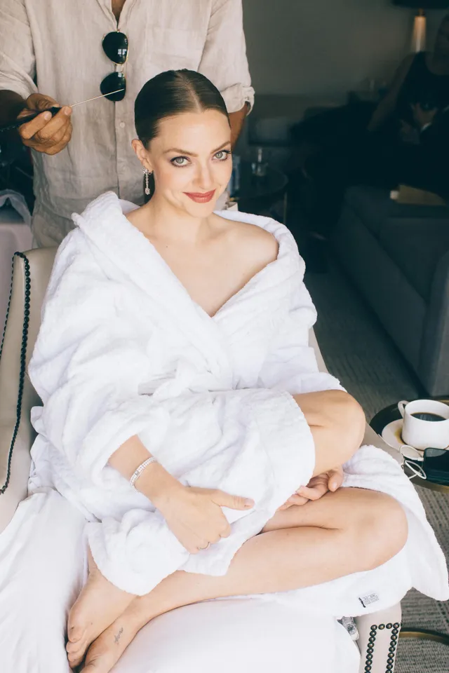 Amanda Seyfried seated barefoot in a white robe with a cup nearby.
