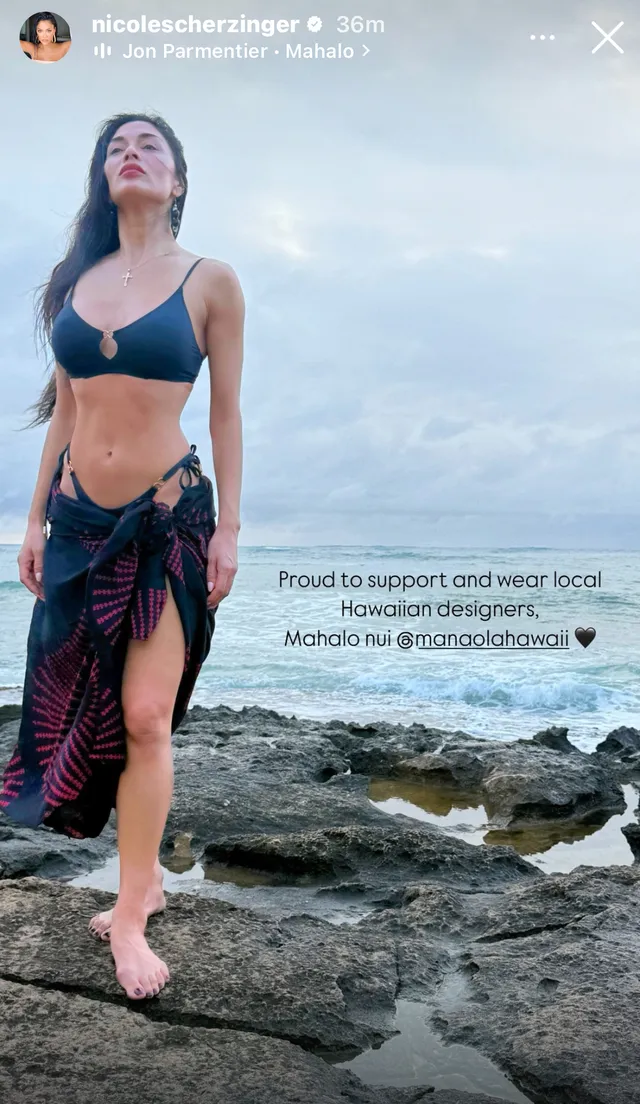 Nicole Scherzinger standing barefoot on coastal rocks.