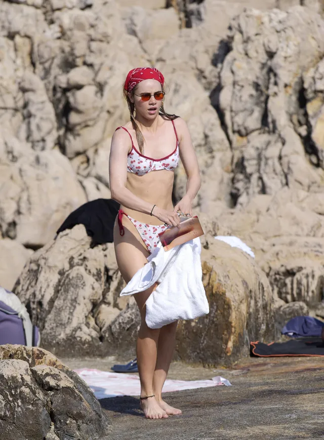 Suki Waterhouse walking near rocks with a towel.