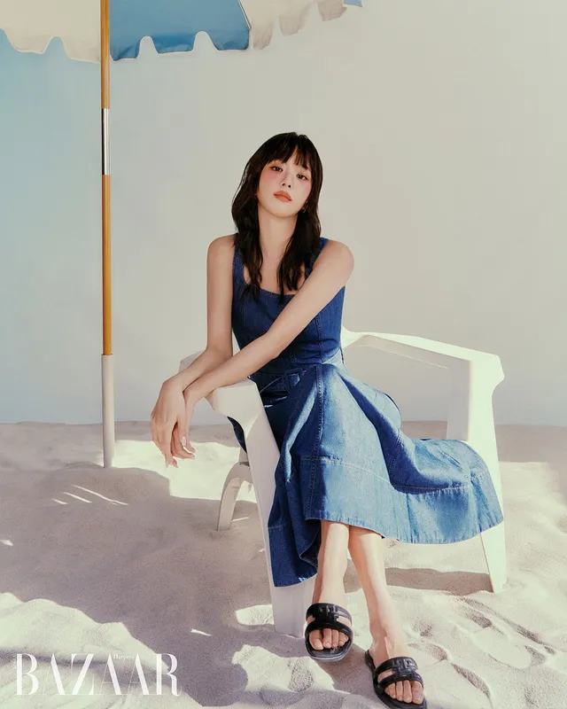 Jisoo sitting on a beach chair wearing black flat slides and a blue dress.