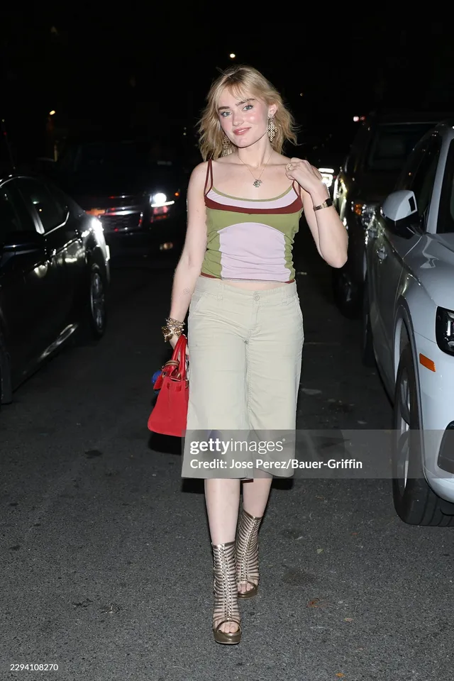 Meg Donnelly walking outdoors in a colorful top, pale skirt and metallic heels.