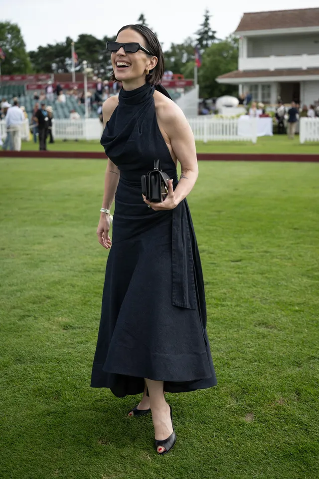 Hayley Atwell standing on a lawn in a black halter dress.