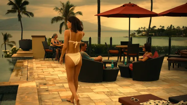 Alexandra Daddario walking barefoot beside a pool at sunset.