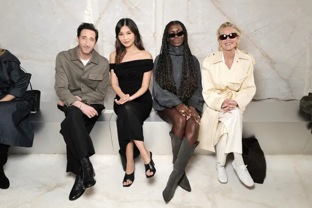 Gemma Chan sitting with guests against a pale wall.
