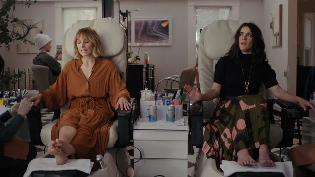 Kristen Bell sitting barefoot at a pedicure station in a screen image.