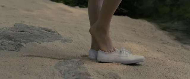 Sophie Thatcher standing with a bare foot resting on a white trainer.