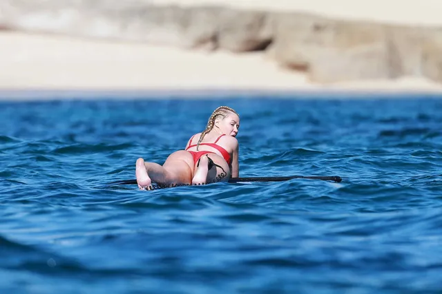 Iggy Azalea lying on a paddleboard with bare soles visible.
