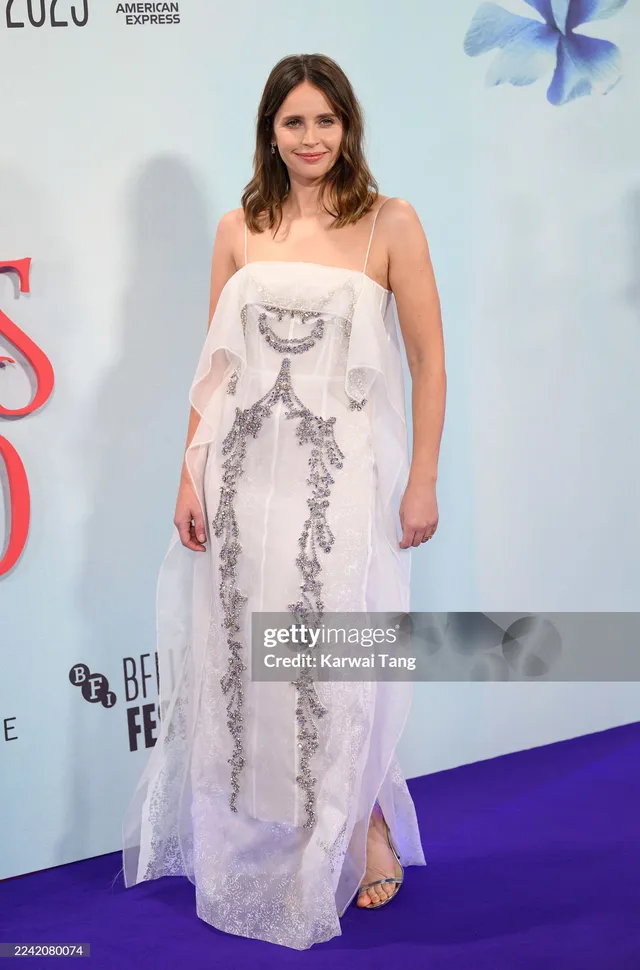 Felicity Jones posing at a film festival in an embellished white gown.
