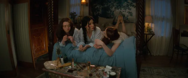 Joey King reclining barefoot beside two people in a film scene.