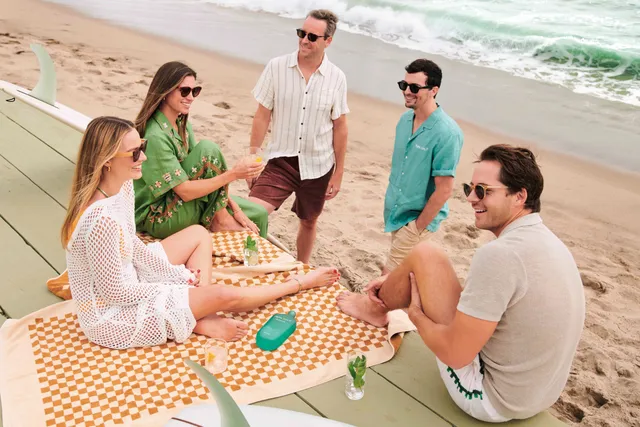 Margot Robbie sitting with friends around a table beside the beach.