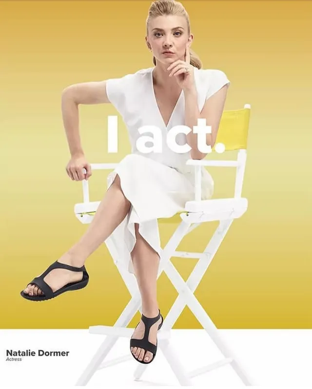 Natalie Dormer sitting in a tall chair in flat black sandals.