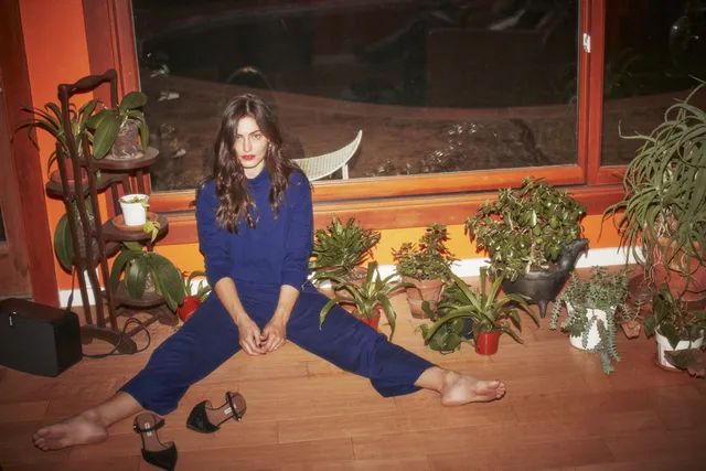 Phoebe Tonkin sitting on a wooden floor in a blue outfit.