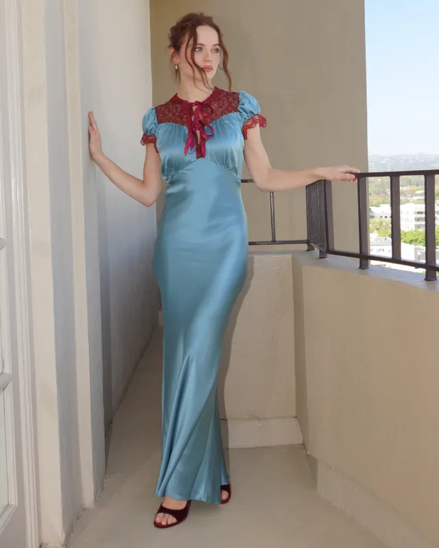 Joey King wearing a blue dress and burgundy heels on a balcony.