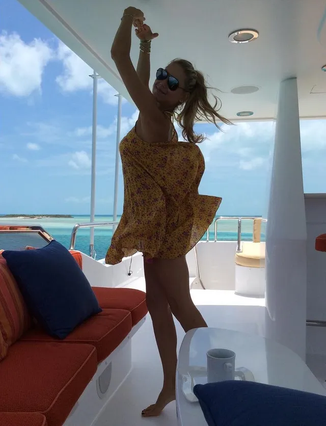 Anna Kournikova standing barefoot on a boat in a yellow patterned cover-up.