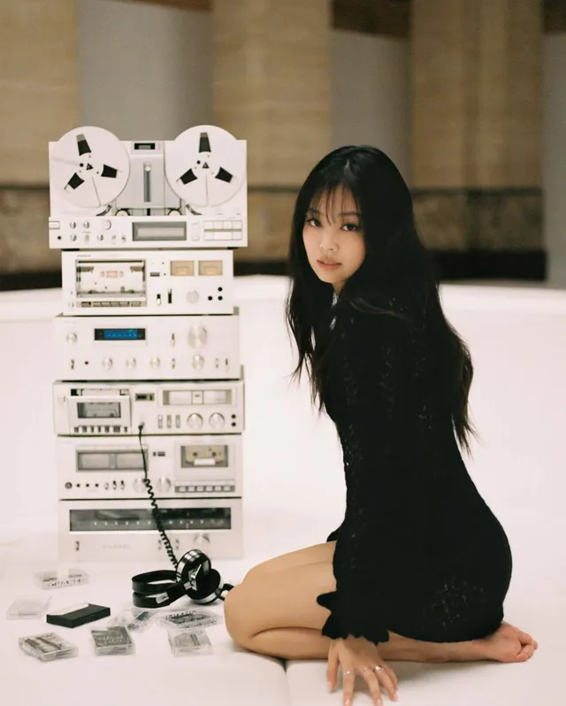 Jennie Kim kneeling barefoot beside recording equipment in a black dress.