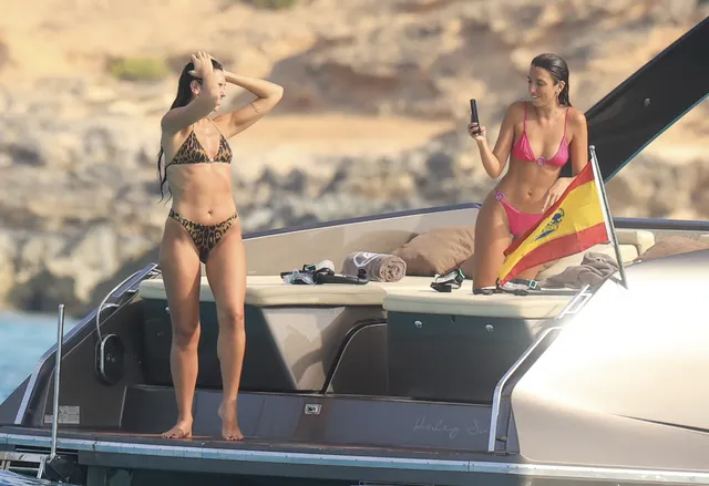 Dua Lipa standing barefoot on a boat beside another woman.