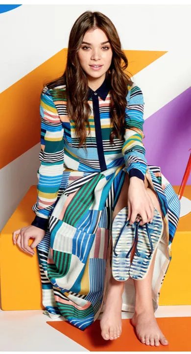Hailee Steinfeld sitting barefoot in a colorful striped dress.