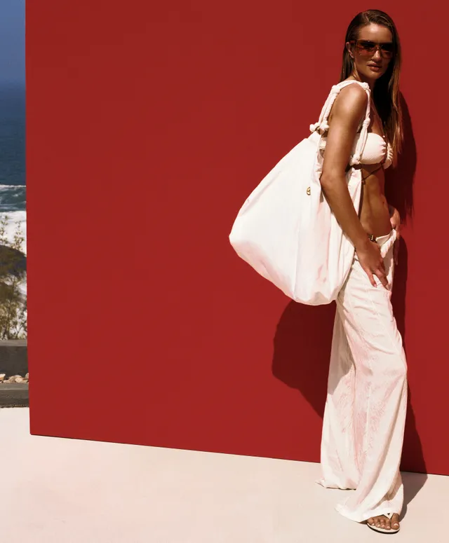 Rosie Huntington-Whiteley posing in pale trousers and heels against a red backdrop.