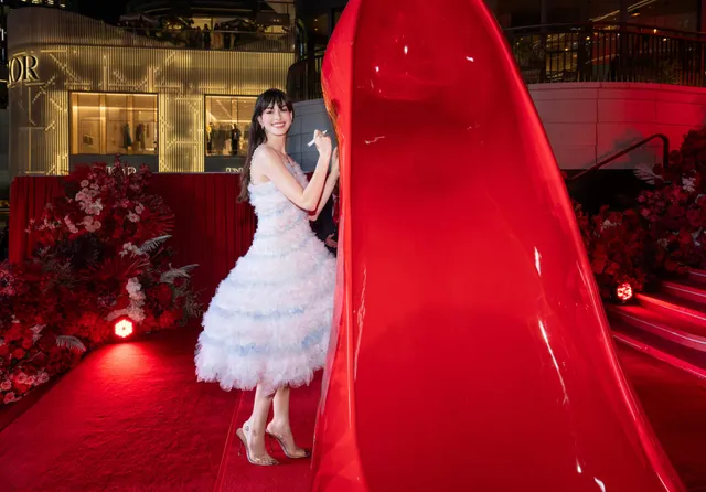 Anne Hathaway posing barefoot on a carpet in a pale feathered dress.