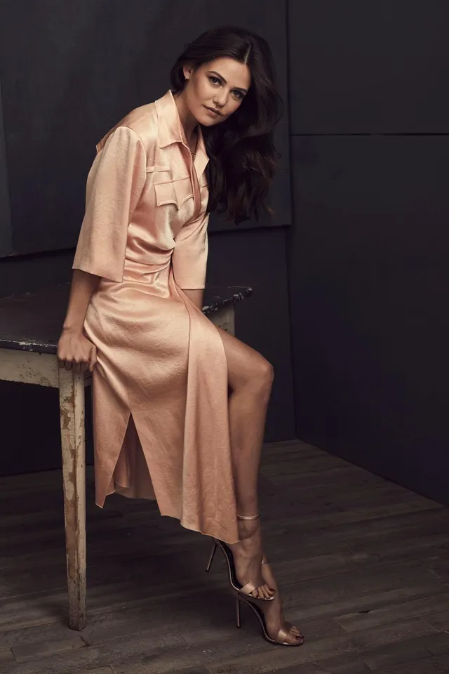 Danielle Campbell posing on a table in a peach satin dress.