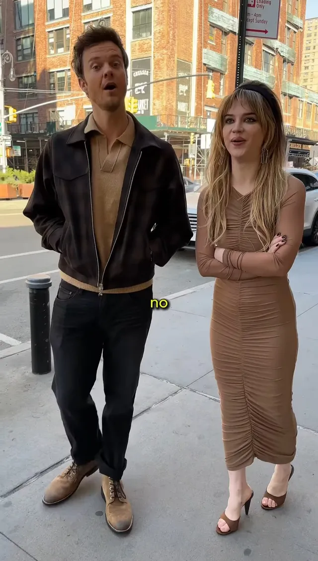 Sophie Thatcher standing beside a man in a fitted dress and heeled sandals.