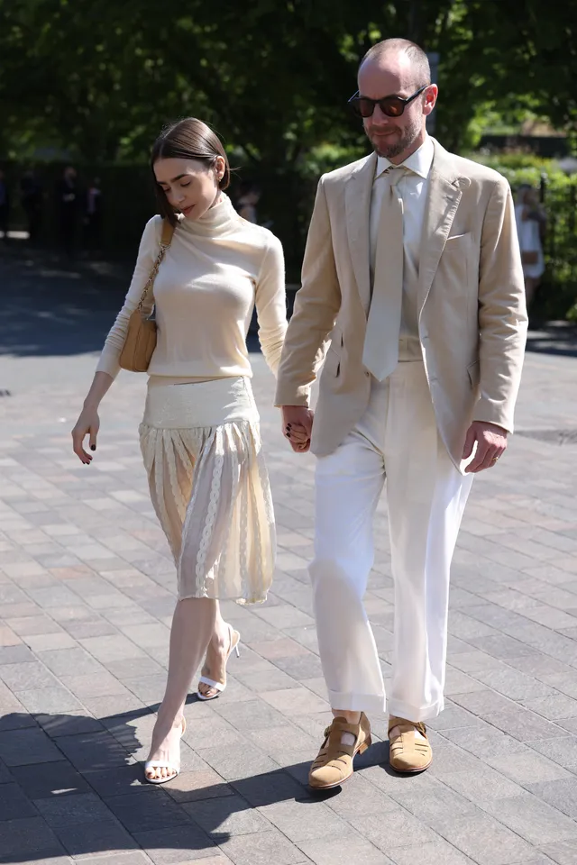 Lily Collins walking beside a man in a cream outfit and heels.