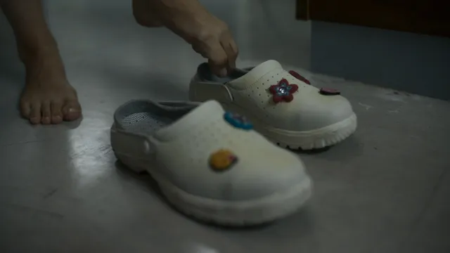 Jodie Comer standing beside decorated clogs in a screen scene.