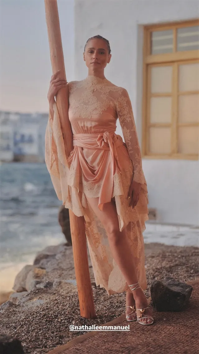 Nathalie Emmanuel posing beside the sea in a pale pink dress.