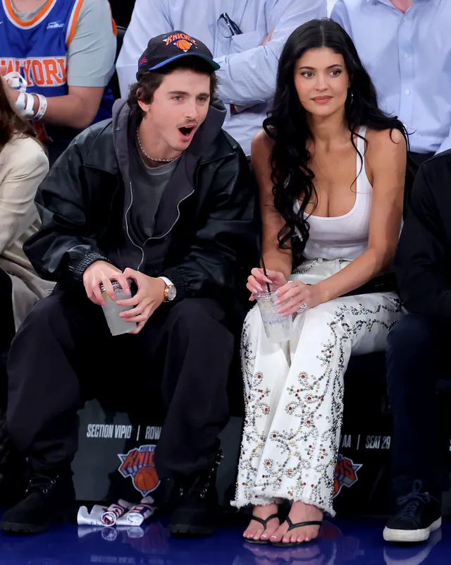 Kylie Jenner sitting beside a companion at a basketball game in flip-flops.